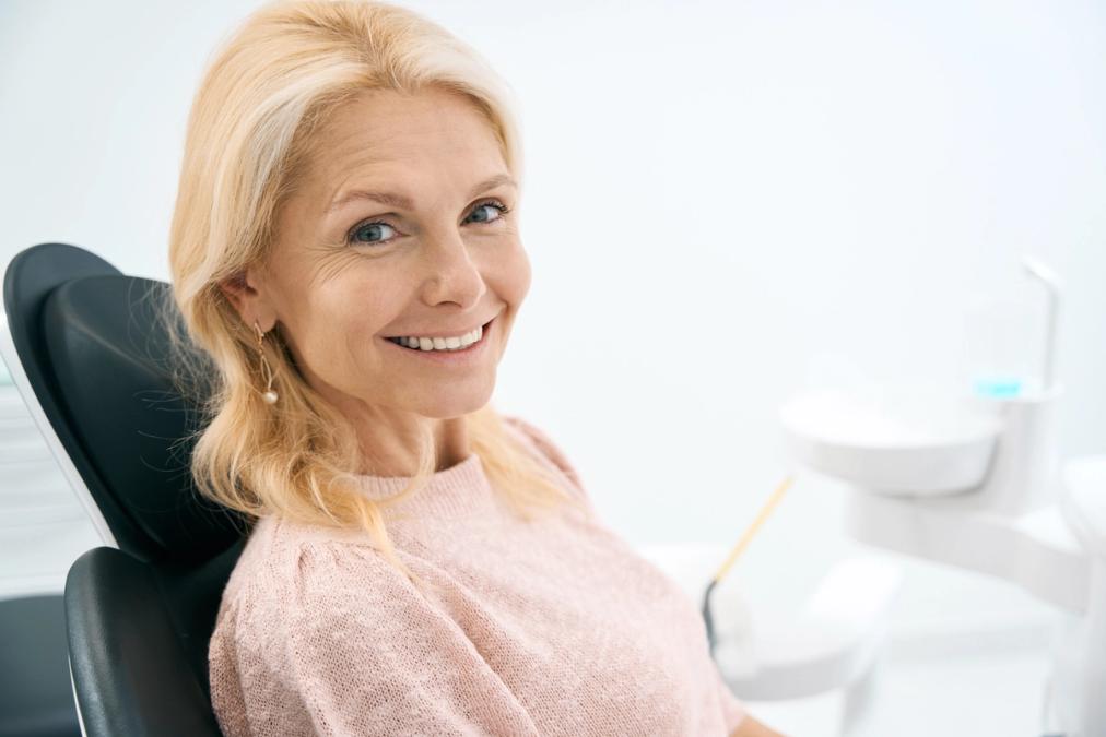 A smiling blonde woman sits in a dental chair.