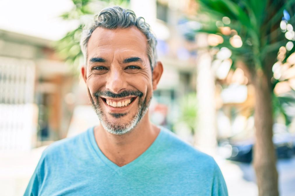 Smiling man with gray hair and beard in a blue shirt outdoors.