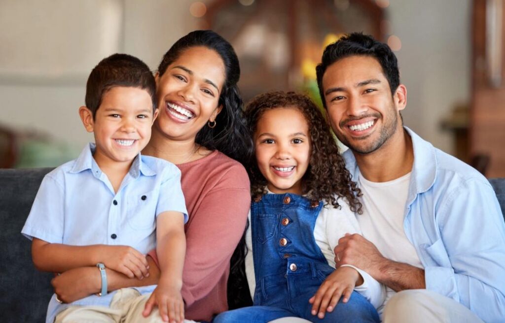 a family is sitting on a couch and smiling for the camera .