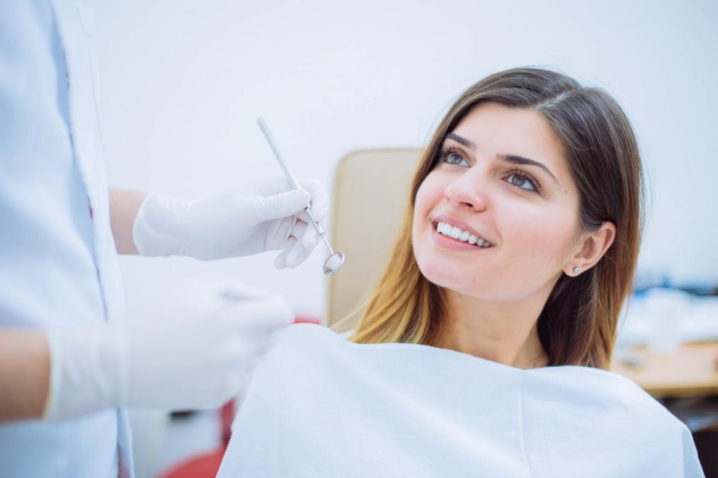 Smiling woman in a dental chair looking up at a dentist holding a dental mirror.