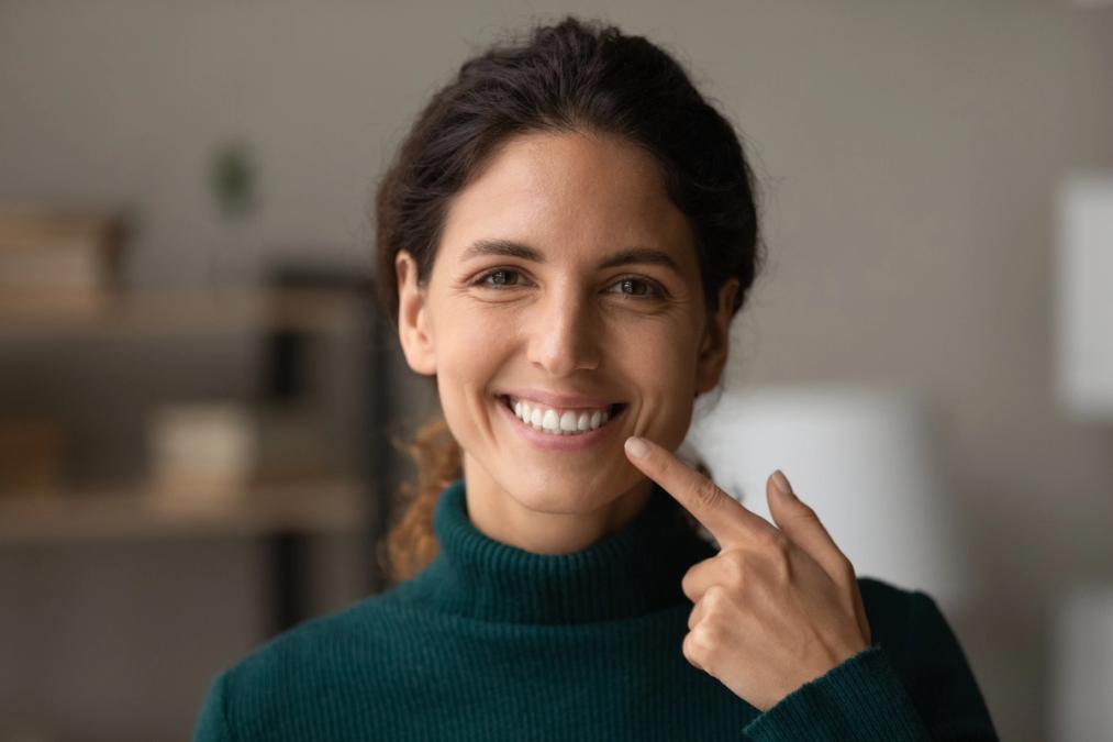 A smiling woman pointing to her teeth.